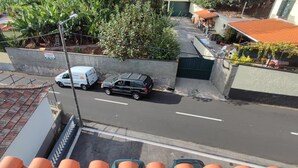 Straßenansicht mit einem weißen Lieferwagen am Straßenrand, einem schwarzen Auto in der Fahrbahn und einem Gebäude mit rotem Dach im Hintergrund.