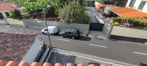 Straßenansicht mit einem weißen Lieferwagen am Straßenrand, einem schwarzen Auto in der Fahrbahn und einem Gebäude mit rotem Dach im Hintergrund.
