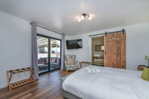 Un dormitorio con cama, televisión, armario de madera y puerta corrediza de vidrio que da a un espacio exterior.