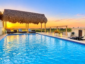 A swimming pool with lounge chairs and a thatched roof structure.