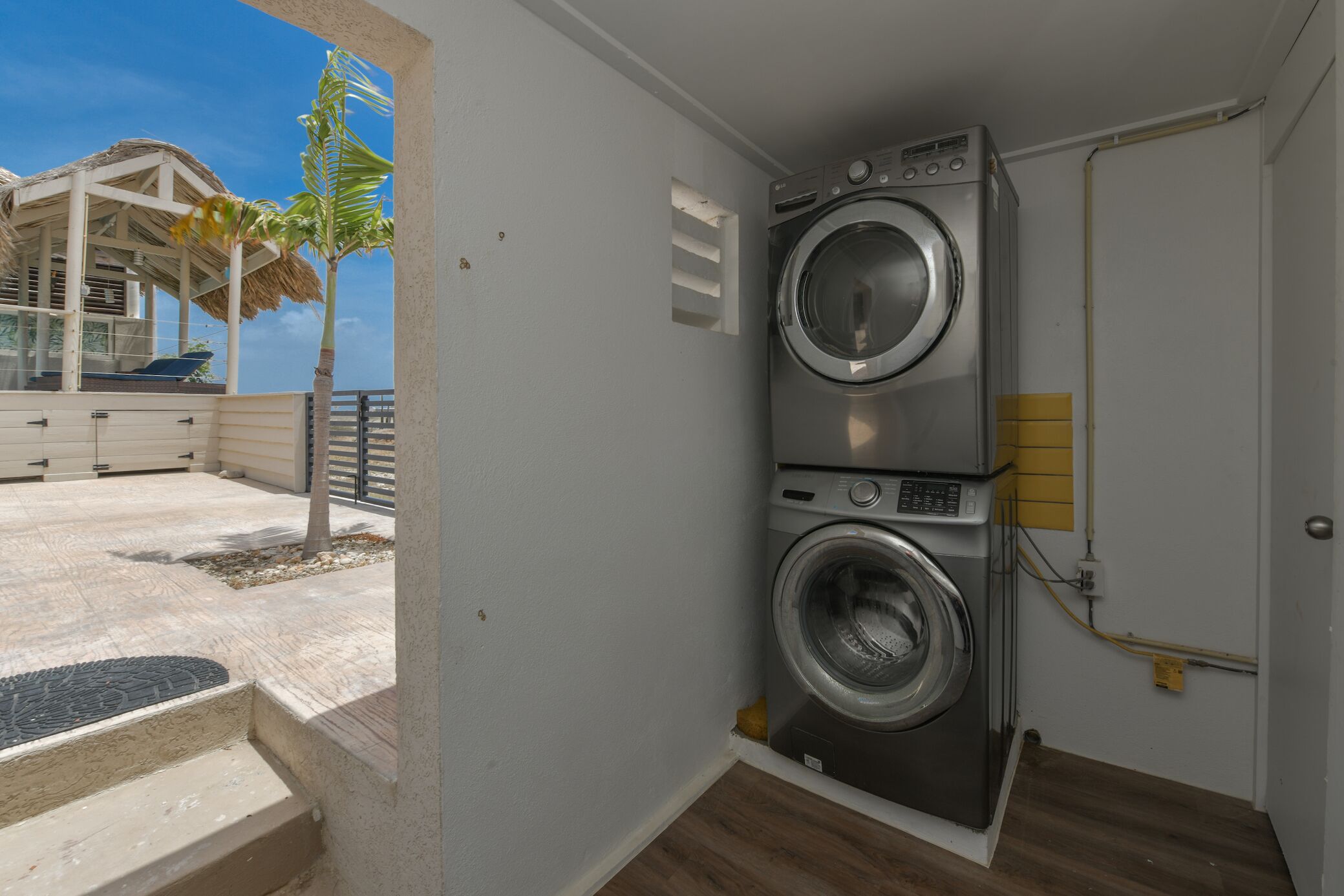 A laundry room with a washing machine, a small step leading to a balcony, and a palm tree outside.