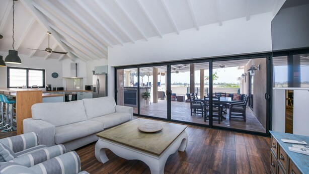 A spacious living area with a large sliding glass door leading to an outdoor patio, a white sofa, striped armchairs, and a wooden coffee table. - Ruby On The Salina: Pool, Bar & Stunning View - 4 Minutes to Beaches! (Noord)