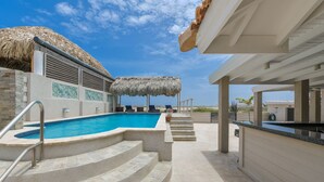 A swimming pool with steps leading up to it, a thatched roof structure, and a covered area with a counter. - Ruby On The Salina: Pool, Bar & Stunning View - 4 Minutes to Beaches! (Noord)