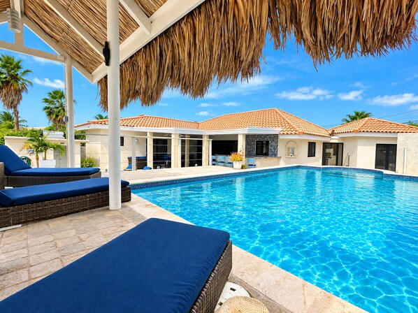 A swimming pool with lounge chairs and a covered area with a thatched roof.