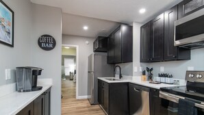 A modern kitchen with dark cabinets, stainless steel appliances, and a coffee bar sign.