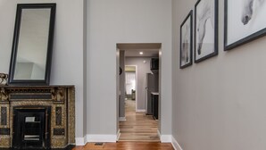 A hallway with a fireplace, framed artwork, and a kitchen area in the distance.