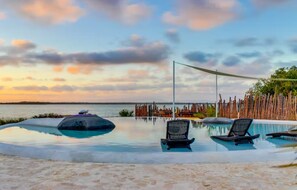 A pool area with lounge chairs and a view of the sea at sunset. - Alterhome Shark Studio (Placencia)
