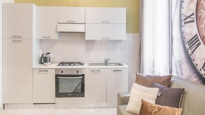 A compact kitchen with white cabinets, a gas stove, and a built-in oven. There's a window with a curtain and a large wall clock. - Venice Grand Canal Style Apt 1 by Wonderful Italy (Venice)