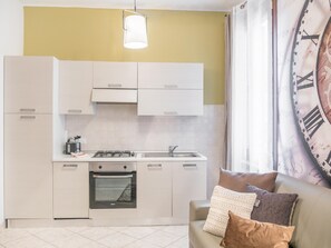 A compact kitchen with white cabinets, a gas stove, and a built-in oven. There's a window with a curtain and a large wall clock. - Venice Grand Canal Style Apt 1 - Locz (Venice)