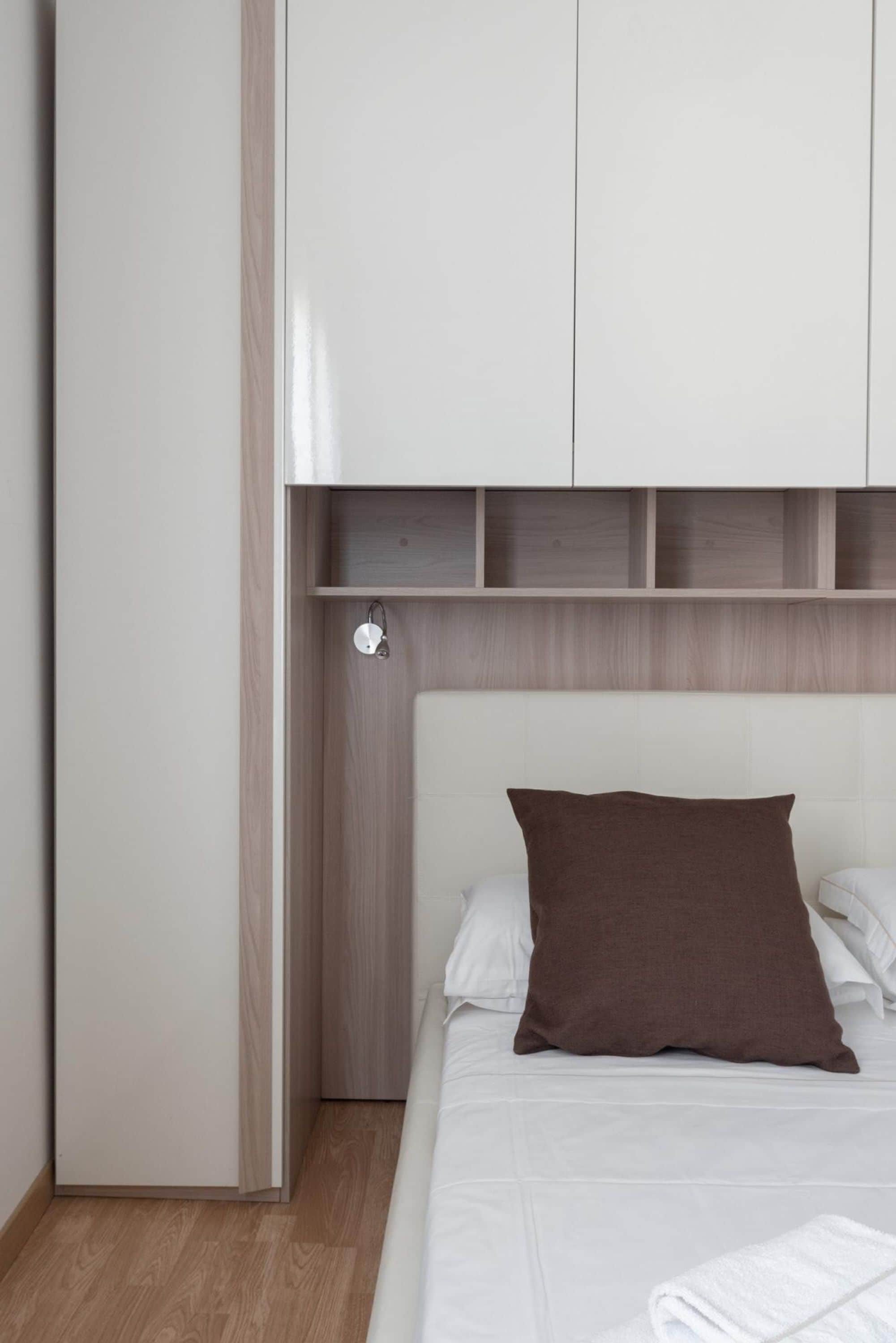 A bedroom with a bed, a brown pillow, a white headboard, and a wooden wardrobe.