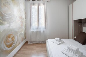 A bedroom with a bed, white curtains, a window, and a wall with a floral mural. - Venice Grand Canal Style Apt 3 by Wonderful Italy (Venice)