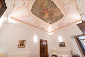 A room with a large ornate ceiling, a wooden door, a bed, and two framed pictures on the walls. - Venice Luxury Palace 12 by Wonderful Italy (Venice)