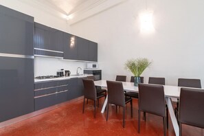 A modern kitchen with grey cabinets, a white countertop, and a red floor. There is a dining table with six chairs and a vase of flowers. - Venice Luxury Palace 12 by Wonderful Italy (Venice)