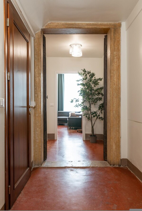 A hallway with a wooden door, a potted plant, and a view into a living area with a sofa and a lamp. - Venice Luxury Palace 12 by Wonderful Italy (Venice)