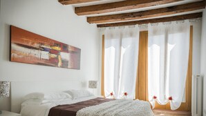 A bedroom with a bed, a nightstand, a painting, and a window with curtains. - Accademia Charm 4 by Wonderful Italy (Venice)
