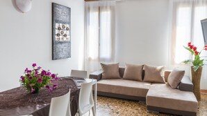 A modern living room with a sectional sofa, a dining table with a vase of flowers, and a large abstract painting on the wall. - Accademia Charm 4 by Wonderful Italy (Venice)