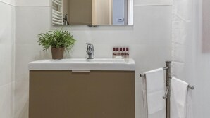 Een badkamer met een wastafel, spiegel, handdoekrek en een plant in pot.