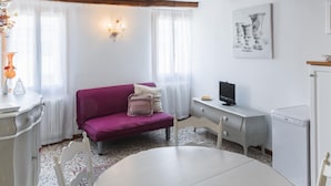 Ein gemütliches Zimmer mit einem violetten Sofa, einem weißen Tisch, einem kleinen Fernseher und einer Waschmaschine.