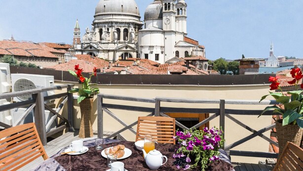 Eine Terrasse mit Frühstückstisch, mit Blick auf historische Gebäude mit Kuppeln und Glockentürmen.