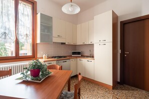 Une cuisine compacte avec des meubles blancs, un four à micro-ondes et une cuisinière. On y trouve une table à manger avec des chaises et une plante en pot.