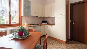 Una cucina funzionale con mobili bianchi, un forno a microonde e un piano cottura. C'è un tavolo da pranzo con sedie e una pianta in vaso.