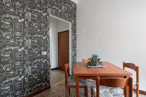 Un coin repas avec une table et des chaises en bois, une plante en pot et un mur orné d’un motif noir et blanc.