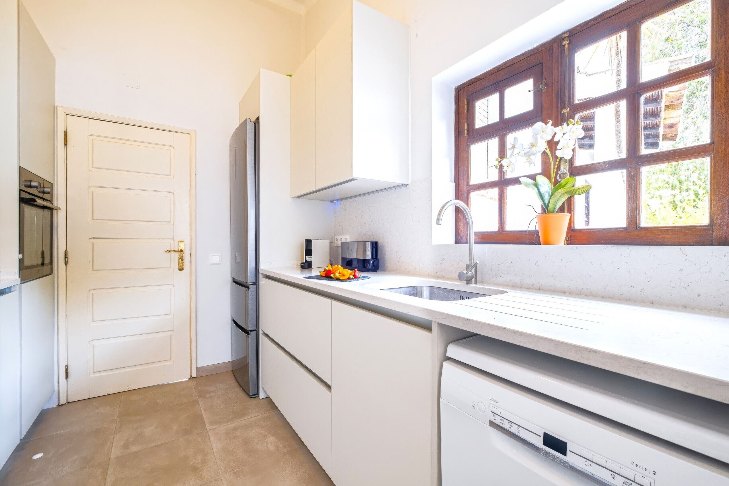 A modern kitchen with white cabinetry, a built-in dishwasher, and a window with a view of greenery.