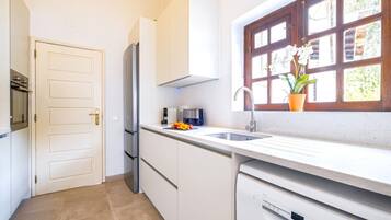 A modern kitchen with white cabinetry, a built-in dishwasher, and a window with a view of greenery.
