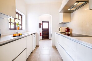 Una cucina stretta con mobili bianchi, una finestra con fiori e una porta che dà su un'altra stanza.