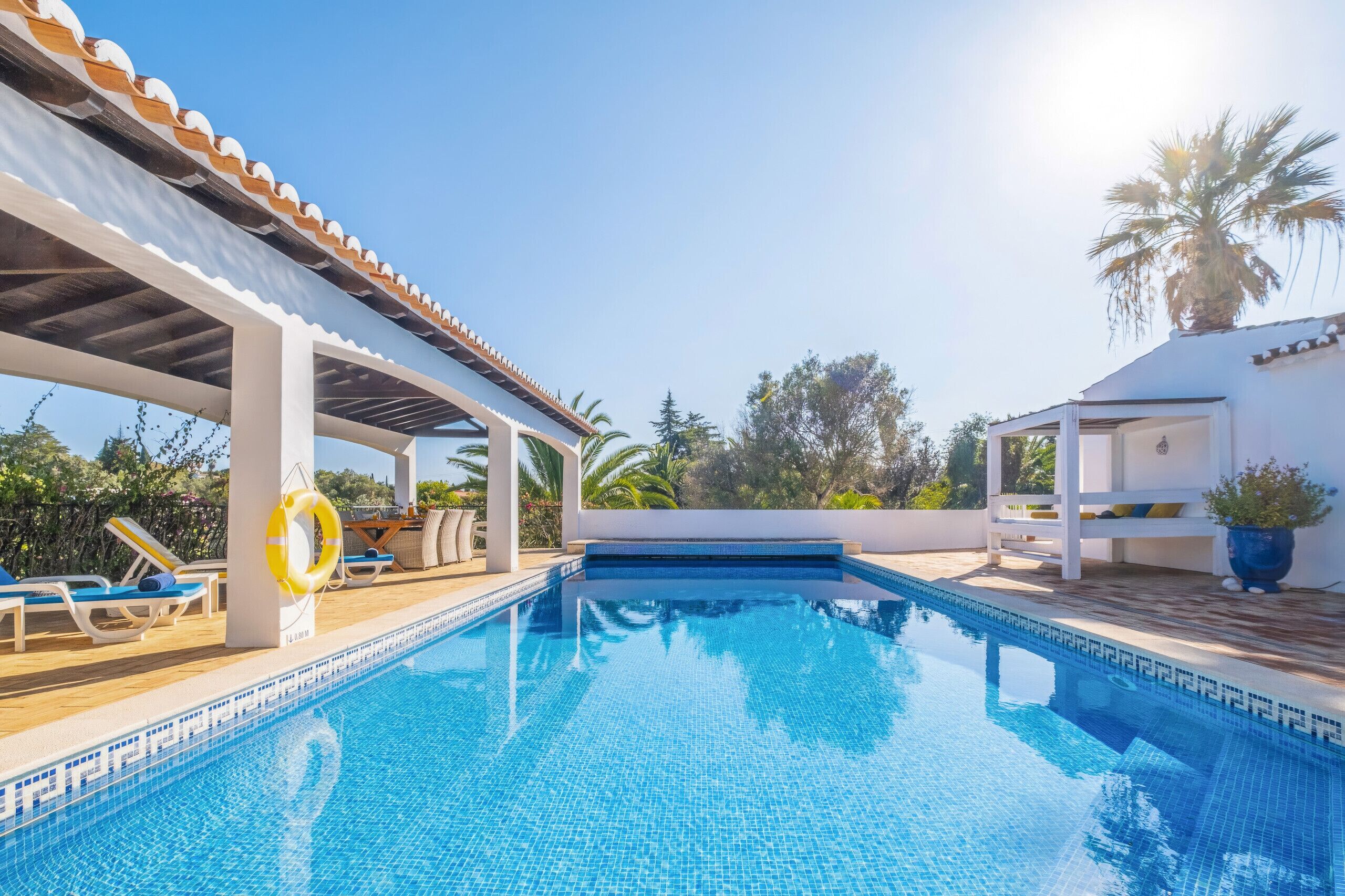A clear blue pool with lounge chairs and a covered seating area.