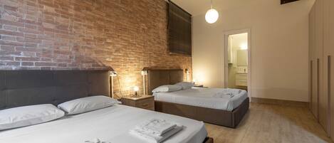 A hotel room with a brick wall, two beds, bedside lamps, and a wooden floor.