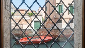 Un étroit canal où est amarré un bateau rouge, devant un bâtiment en briques orné de volets verts.