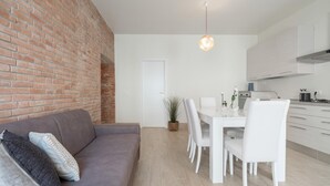 Une cuisine moderne avec des meubles blancs, une table à manger avec des chaises et un mur en briques.