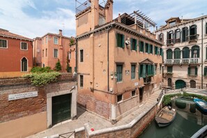 Un bâtiment situé au bord d’un canal, avec une façade en briques, une entrée bien visible et un petit bateau amarré à proximité.