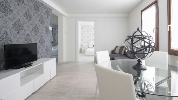 A modern living room with a flat-screen TV on a white console, a glass dining table with chairs, and a decorative globe on a stand. - San Marco Style Canal View Apt 1 by Wonderful Italy (Venice)