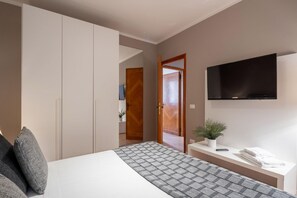 Een slaapkamer met een bed, een aan de muur bevestigde televisie, een nachtkastje met een plant en een deur naar een andere kamer.