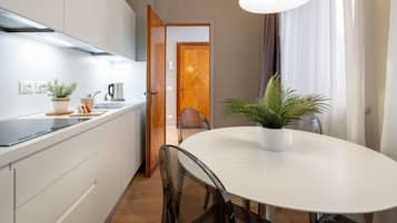 A modern kitchen with white cabinets, a black countertop, and a white dining table with chairs.