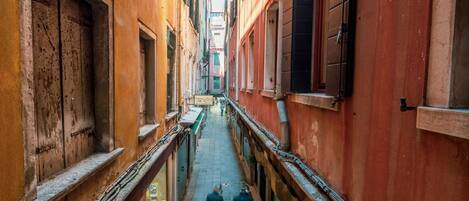 A narrow alleyway with buildings on either side, featuring a wooden door and a window with a sign.