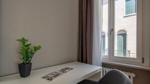 A room with a white desk, a potted plant, and a window with curtains. - San Marco Suite 1 by Wonderful Italy (Venice)