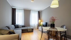 A modern living room with a sofa, a coffee table, and a dining table with chairs. There is a TV and a lamp on the coffee table. - San Marco Suite 1 by Wonderful Italy (Venice)