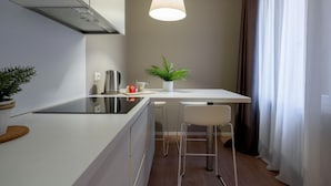 A compact kitchen with a modern stove, a kettle, and a small table with two chairs. There is a potted plant on the table and a hanging light fixture above. - San Marco Suite 1 by Wonderful Italy (Venice)
