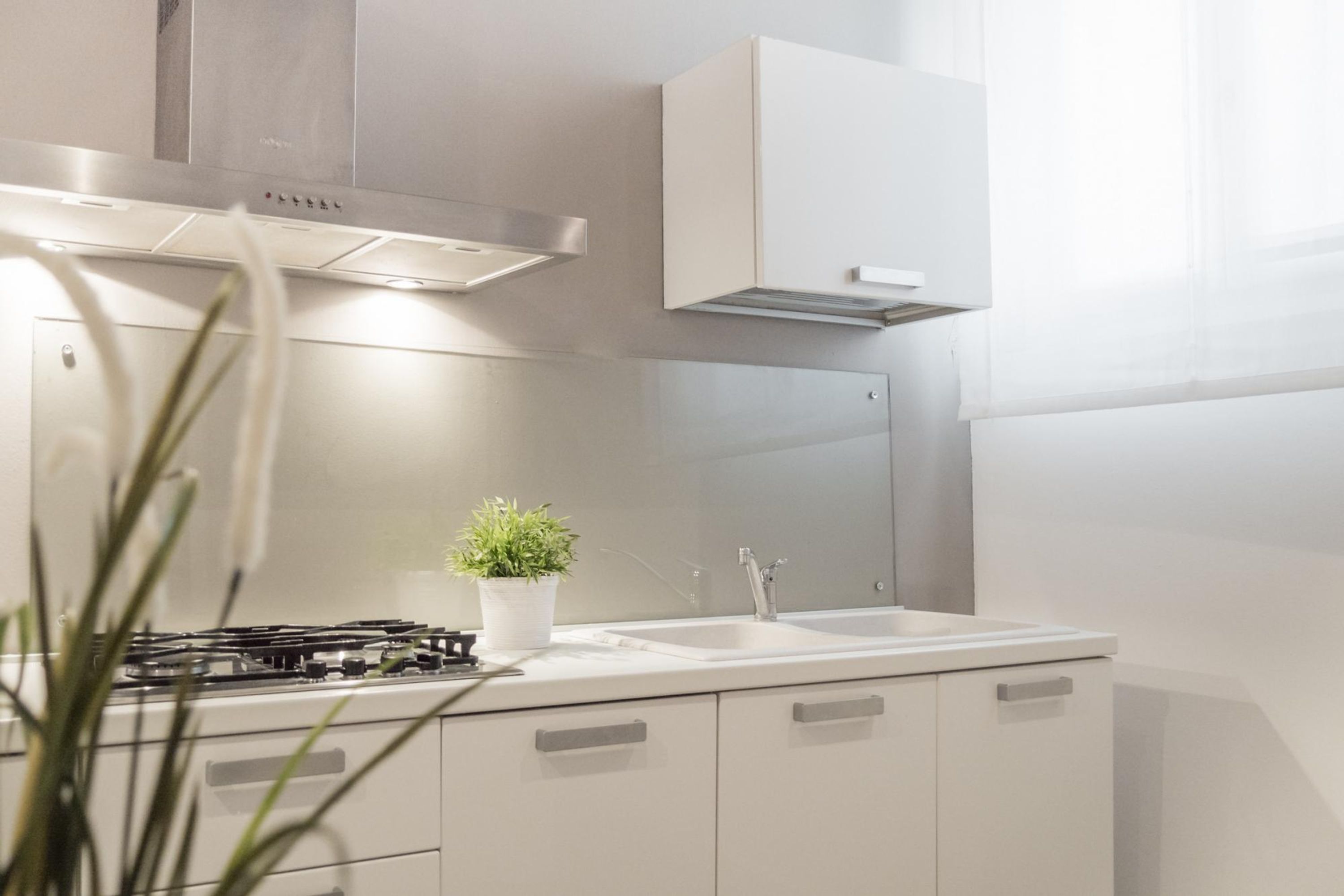 A modern kitchen with a gas stove, a sink, cabinets, and a stainless steel range hood.