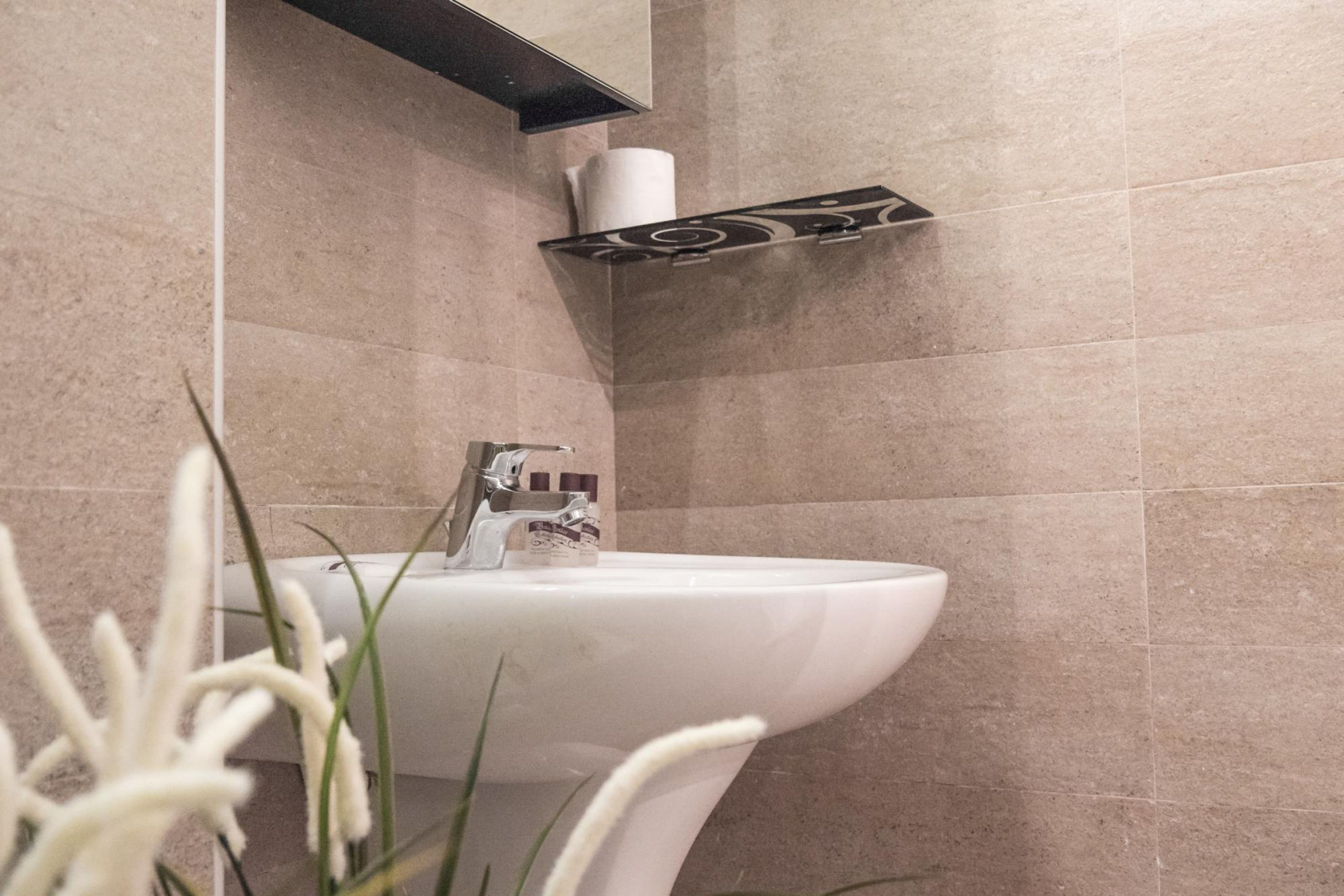 A bathroom with a white sink, a towel dispenser, and a toilet paper holder on the wall.