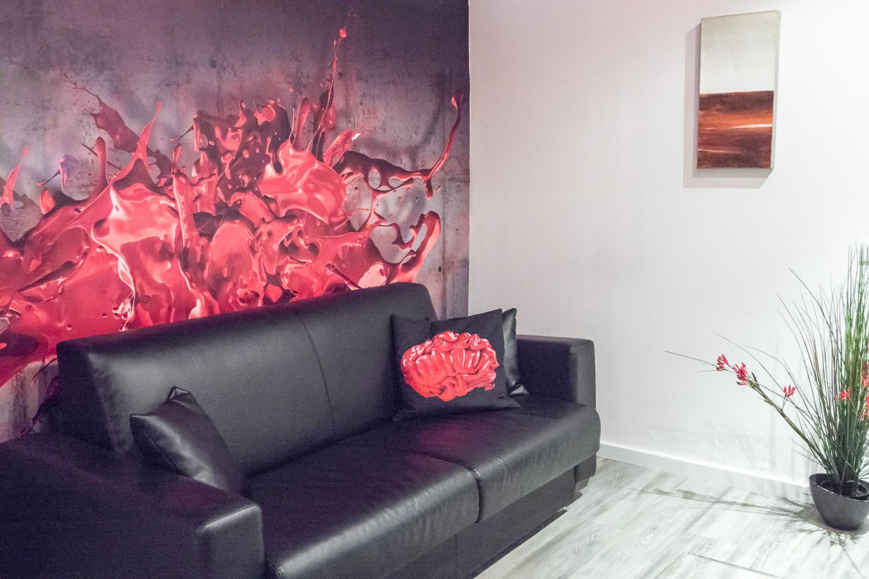 Una sala de estar moderna con un sofá de cuero negro, un cojín con forma de cerebro rojo, un cuadro abstracto de gran tamaño y una planta en maceta.