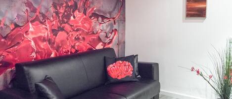 Una sala de estar moderna con un sofá de cuero negro, un cojín con forma de cerebro rojo, un cuadro abstracto de gran tamaño y una planta en maceta.