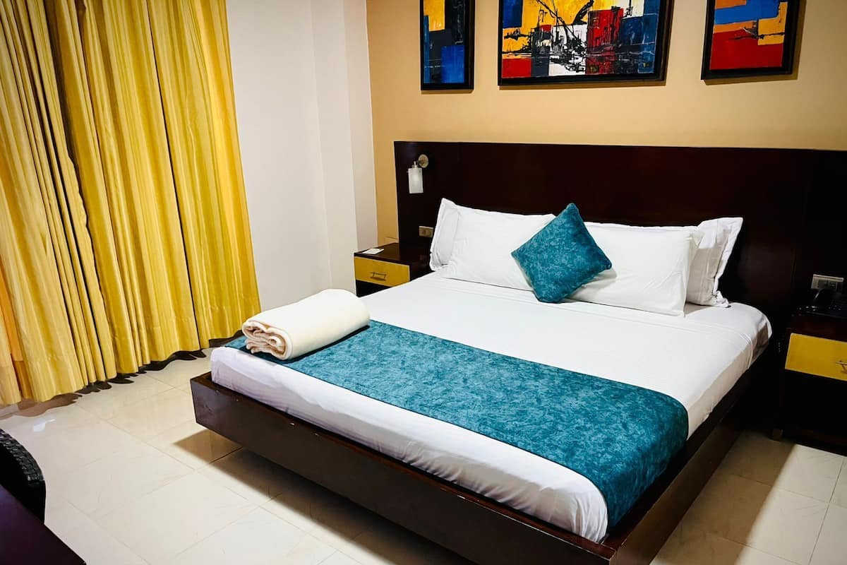 A hotel room with a large bed, a wooden headboard, a nightstand, and a yellow curtain.