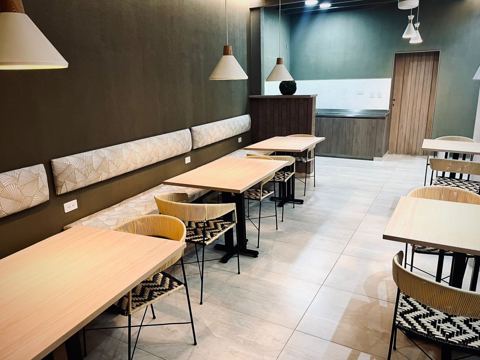 A modern restaurant with wooden tables and chairs, a long bench, and pendant lighting.