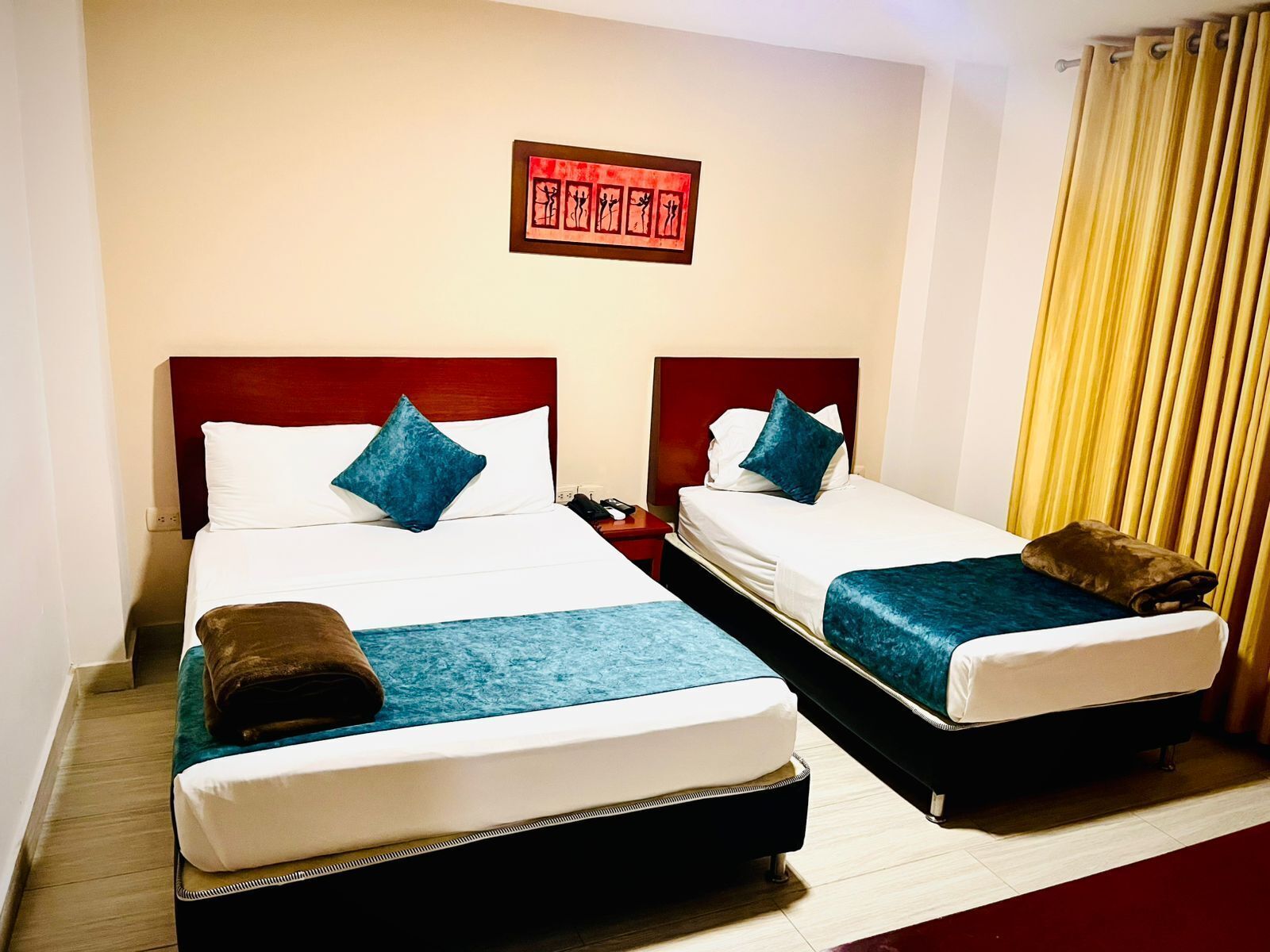 A hotel room with two beds, each with a headboard, white bedding, and blue throw pillows. There is a framed artwork on the wall above the beds.