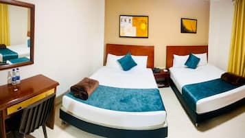 Habitación de hotel con dos camas, una mesita de noche con lámpara, un espejo y obras de arte en las paredes.