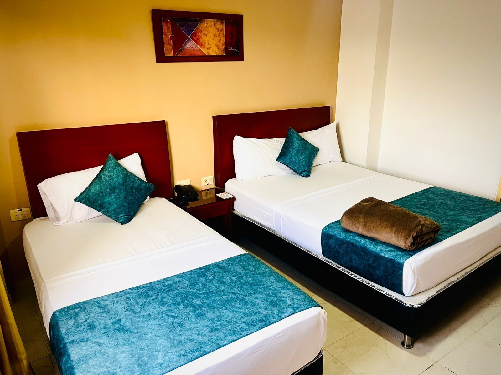 Two single beds with matching headboards and footboards, a bedside table with a phone, and a wall-mounted artwork.
